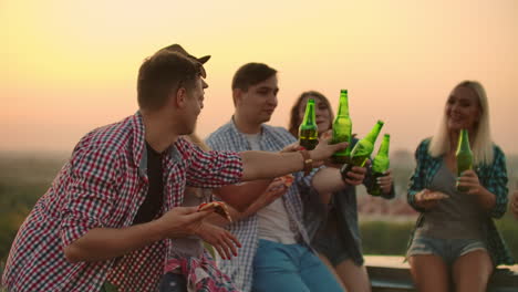 A-man-raises-a-toast-to-a-friend's-birthday-in-friends-company-on-the-roof.-They-clink-beer-and-eat-pizza.